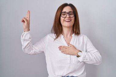 Brunette woman standing over white isolated background smiling swearing with hand on chest and fingers up, making a loyalty promise oath 