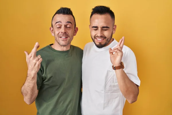 Homosexual Couple Standing Yellow Background Gesturing Finger Crossed Smiling Hope — Stockfoto