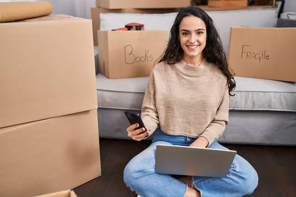 年轻的惊慌失措的女人坐在新家的地板上 用笔记本电脑和智能手机 — 图库照片