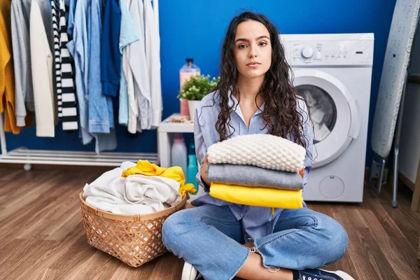 stock image Young brunette woman holding clean laundry relaxed with serious expression on face. simple and natural looking at the camera. 