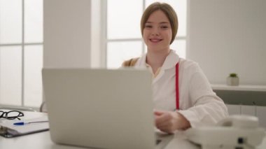 Klinikte doktor üniforması giyen genç sarışın kadın.