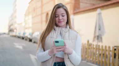 Sokakta akıllı telefon kullanan, kendine güvenen genç sarışın kadın.