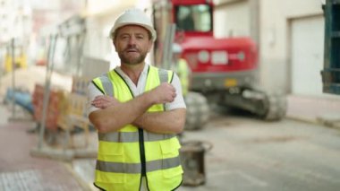 Orta yaşlı mimar gülümsüyor. Kollarını kavuşturup caddede duruyor.