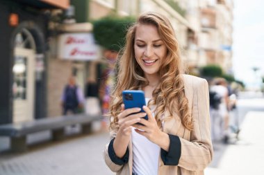 Sokakta akıllı telefon kullanan, kendine güvenen genç sarışın kadın.