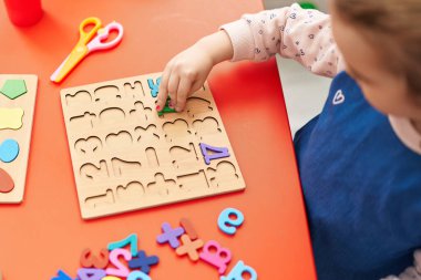 Adorable blonde girl playing with maths puzzle game sitting on table at kindergarten