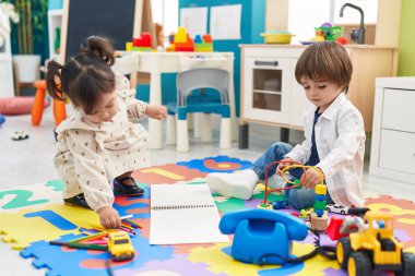 Two kids drawing and playing with cars toy sitting on floor at kindergarten