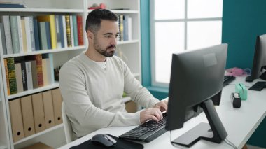 Young hispanic man student using computer studying at library university