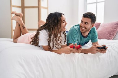 Young hispanic couple playing video game lying on bed at bedroom