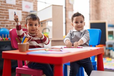 Two kids preschool students sitting on table drawing on paper at kindergarten