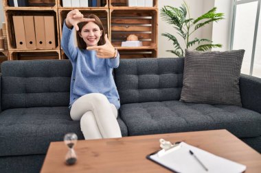 Young brunette woman at consultation office smiling making frame with hands and fingers with happy face. creativity and photography concept. 