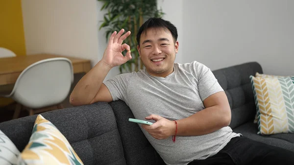 若いです中国人男使用スマートフォン行いますOkジェスチャーでホーム — ストック写真