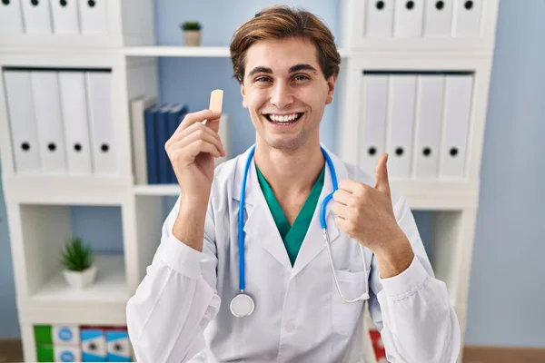 Młody Lekarz Człowiek Trzymając Bandaż Uśmiecha Szczęśliwy Pozytywny Kciuk Góry — Zdjęcie stockowe