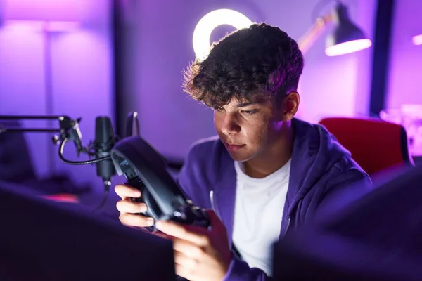 Young Hispanic Teenager Streamer Holding Headphones Relaxed Expression Gaming Room — Stockfoto