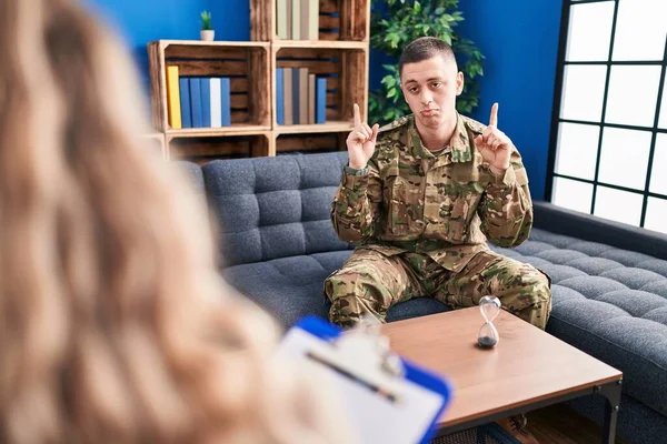 Young man doing therapy after war pointing up looking sad and upset, indicating direction with fingers, unhappy and depressed.