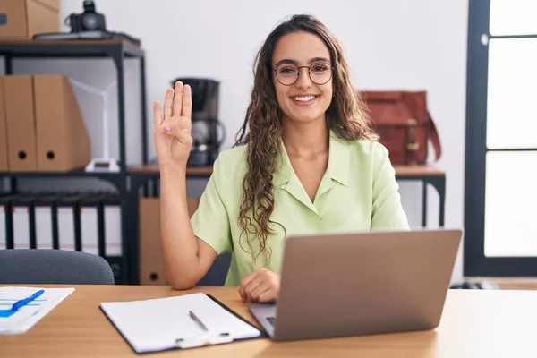 stock image Young hispanic woman working at the office wearing glasses showing and pointing up with fingers number four while smiling confident and happy. 