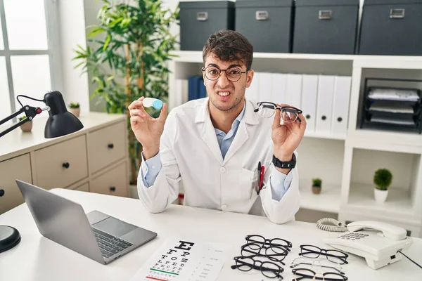 Young Hispanic Oculist Holding Glasses Contact Lenses Clueless Confused Expression — Stockfoto