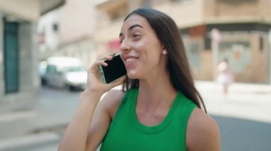 Genç, güzel, İspanyol bir kadın gülümsüyor ve caddede akıllı telefondan konuşuyor.