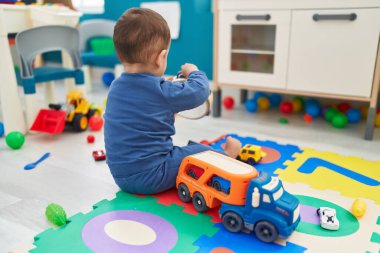 Anaokulunda yerde oturmuş tef çalan sevimli İspanyol çocuk.