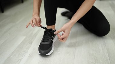 Young beautiful hispanic woman tying shoe at sport center