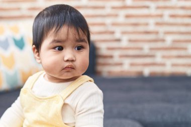 Adorable hispanic baby sitting on sofa with relaxed expression at home