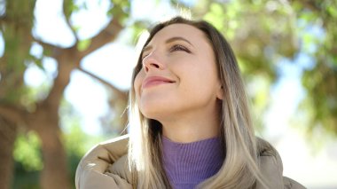 Young blonde woman smiling confident looking to the sky at park