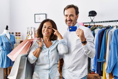 Hispanic middle age couple holding shopping bags and credit card smiling pointing to head with one finger, great idea or thought, good memory 