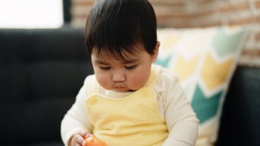 Adorable hispanic baby sitting on sofa with relaxed expression at home