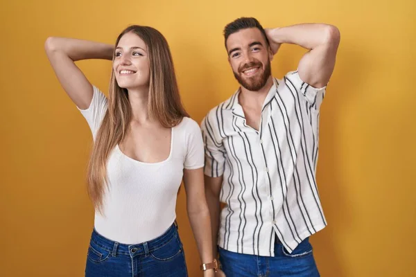 Sarı Arka Planda Duran Genç Çift Gülümsüyor Hareketleriyle Saçlarına Dokunuyor — Stok fotoğraf