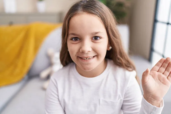 Adorable Hispanic Girl Sitting Sofa Saying Hello Hand Home — Stockfoto