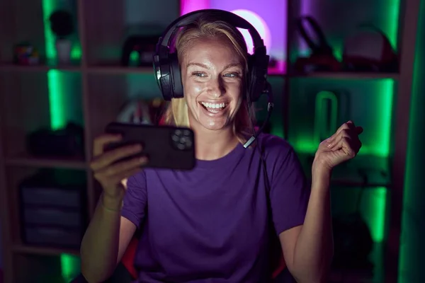 Young gamer woman playing video games with smartphone screaming proud, celebrating victory and success very excited with raised arm