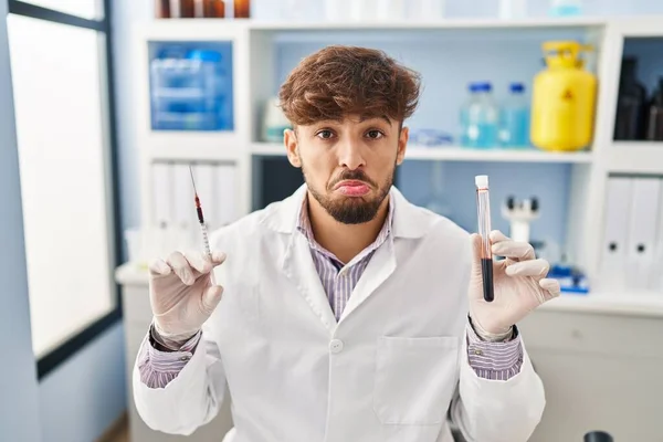 Arab man with beard working at scientist laboratory holding blood sample depressed and worry for distress, crying angry and afraid. sad expression.
