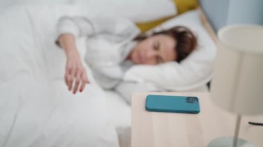 Middle age woman sleeping turning off smartphone alarm at bedroom