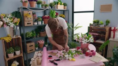 Young redhead man florist make bouquet of flowers at flower shop