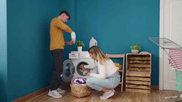 若いカップルは洗濯室で自信を持って洗濯服を笑って — ストック動画