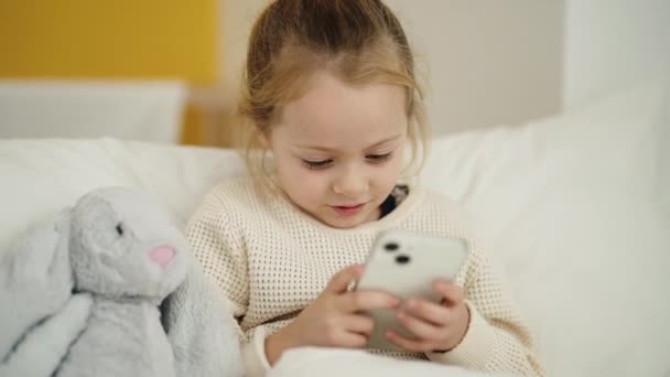 Αξιολάτρευτο Ξανθό Κορίτσι Που Χρησιμοποιεί Smartphone Κάθεται Στο Κρεβάτι Στο — Αρχείο Βίντεο
