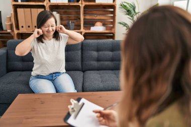 Hispanic girl with down syndrome doing therapy covering ears with fingers with annoyed expression for the noise of loud music. deaf concept. 