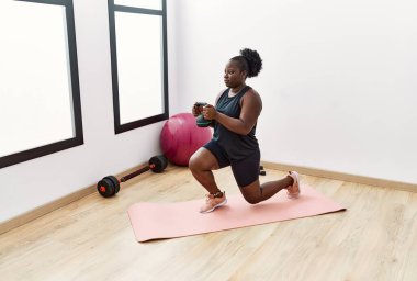 Genç Afrikalı Amerikalı kadın spor merkezinde dambıl kullanıyor.