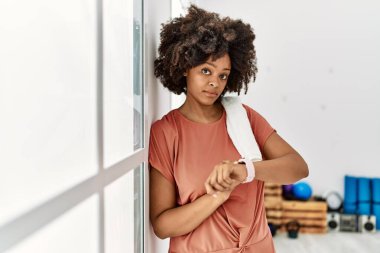 Genç Afrikalı Amerikalı kadın spor merkezinde duvara yaslanmış saati izliyor.