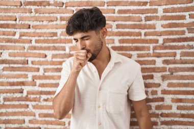 Arab man with beard standing over bricks wall background feeling unwell and coughing as symptom for cold or bronchitis. health care concept. 