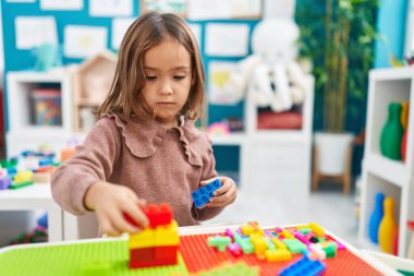 Anaokulundaki masada oturan, inşaat bloklarıyla oynayan sevimli İspanyol kız.