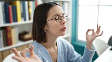 Young beautiful hispanic woman student doing yoga exercise at library university