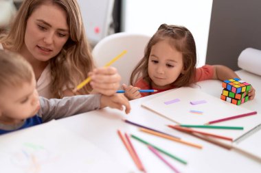 Teacher with boy and girl sitting on table drawing on paper at kindergarten