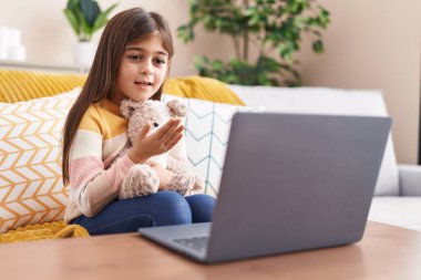 Adorable hispanic girl having video call sitting on sofa at home