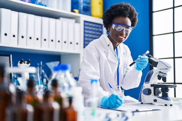 Young African American Woman Scientist Writing Document Holding Blood Analysis — ストック写真