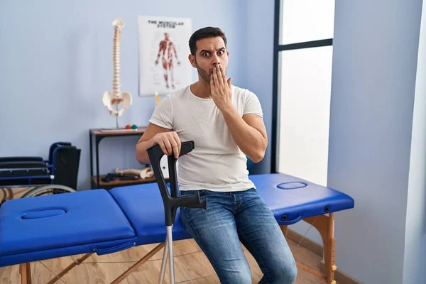 Young Hispanic Man Beard Wearing Crutches Rehabilitation Clinic Covering Mouth — Fotografia de Stock