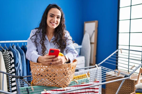 Young Hispanic Woman Using Smartphone Standing Laundry Room — Fotografia de Stock