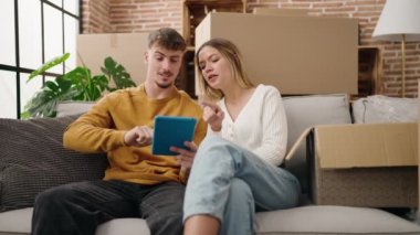 Young couple using touchpad sitting on sofa at new home