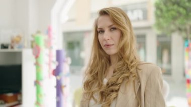 Genç sarışın bayan mağazada kollarını kavuşturup gülümsüyor.