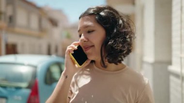 Gülümseyen genç bir kadın caddedeki akıllı telefondan konuşuyor.