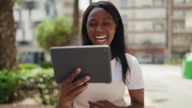Genç Afrikalı Amerikalı kadın gülümsüyor. Parktaki dokunmatik ekranda kendine güvenen bir şekilde videoyu izliyor.
